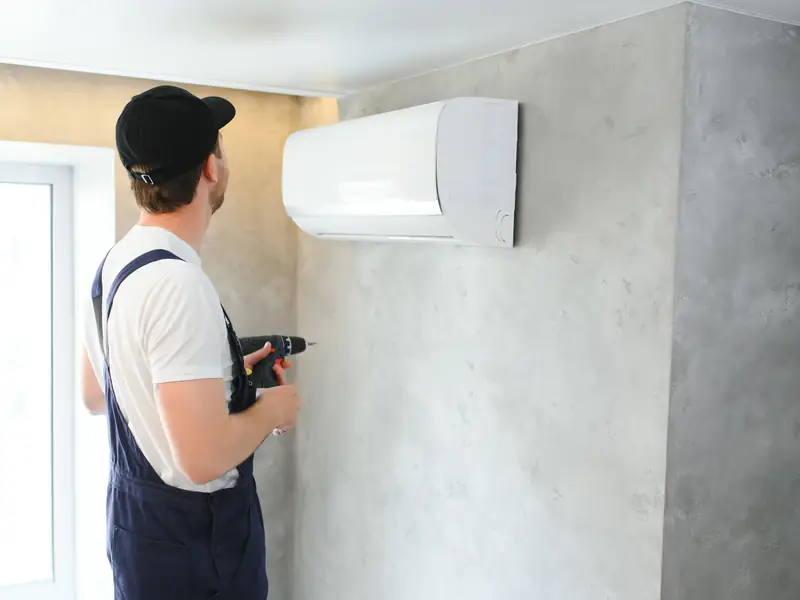 Installateur fixant une unité murale de climatisation au mur d'une pièce