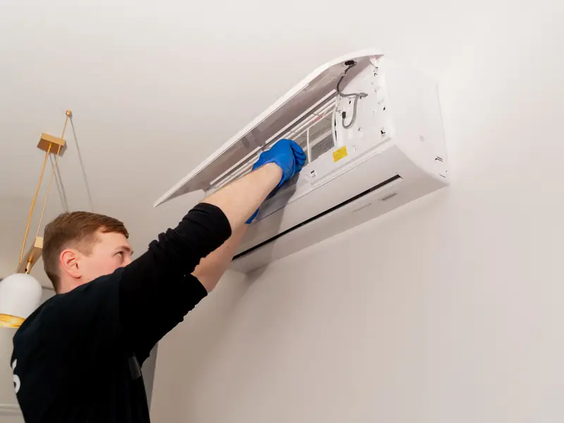 Technicien nettoyant une unité murale de climatisation encrassée